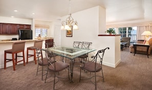 A spacious kitchen with dark wooden cabinets, a black refrigerator, and a glass dining table surrounded by four chairs.