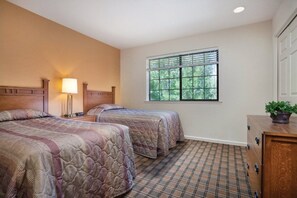 Une chambre d’hôtel avec deux lits, une fenêtre avec des stores, une commode et une lampe.
