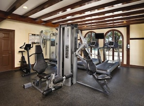 Une salle de sport équipée de tapis de course, d’appareils de musculation et d’un téléviseur fixé au mur.