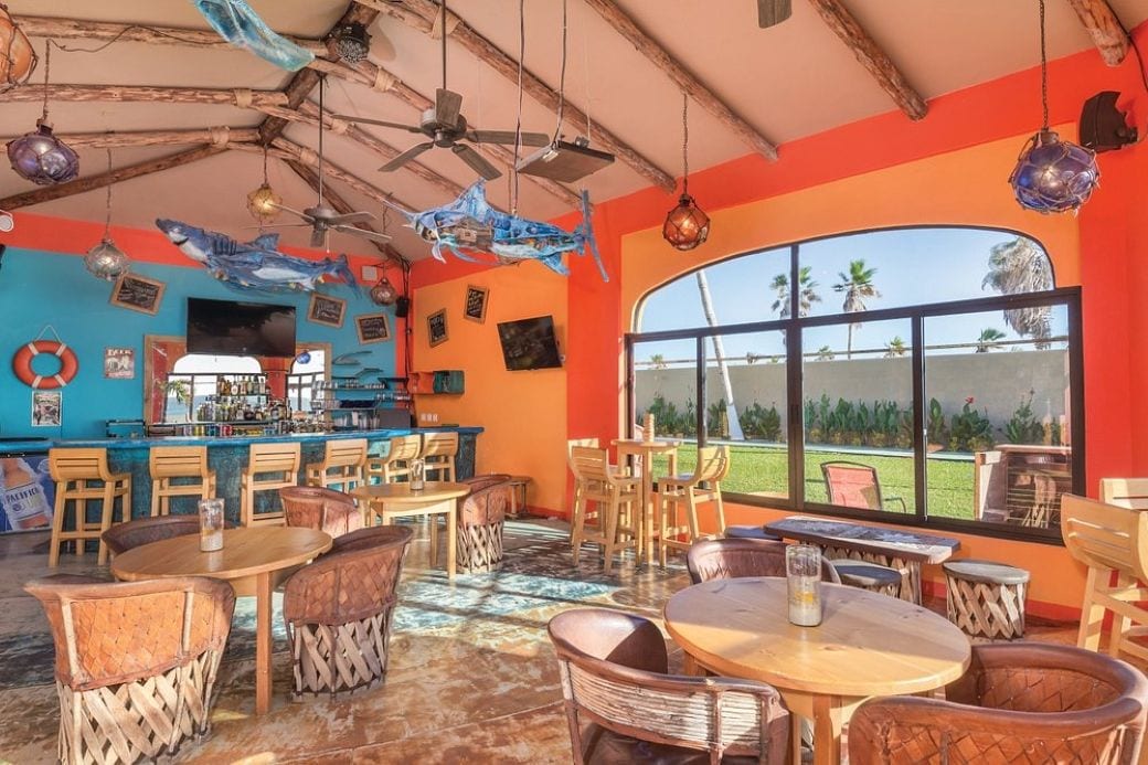 A restaurant with a bar, outdoor seating, and a view of palm trees.