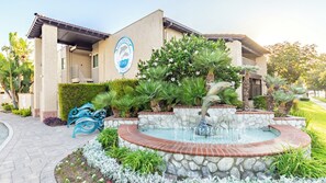 A building with a dolphin logo, a fountain, and a paved walkway. - Anaheim | Romantic Disney Retreat | Pool + Parks (Anaheim)