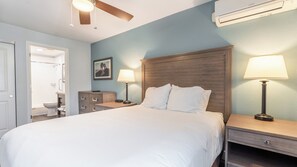 Una camera da letto ordinata con un letto grande, due comodini con lampade, una testiera in legno, una ventola a soffitto e un condizionatore d'aria.