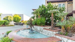 A swimming pool with a dolphin sculpture, surrounded by palm trees and a stone wall. - Anaheim | Family Disney Retreat | Pool + Parks | 3BR Sleeps 8 (Anaheim)