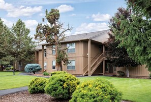 A multi-story building with a staircase leading to the entrance, surrounded by well-maintained lawns and various trees. - Redmond | High Desert Comfort Escape | Pool + Trails (Redmond)