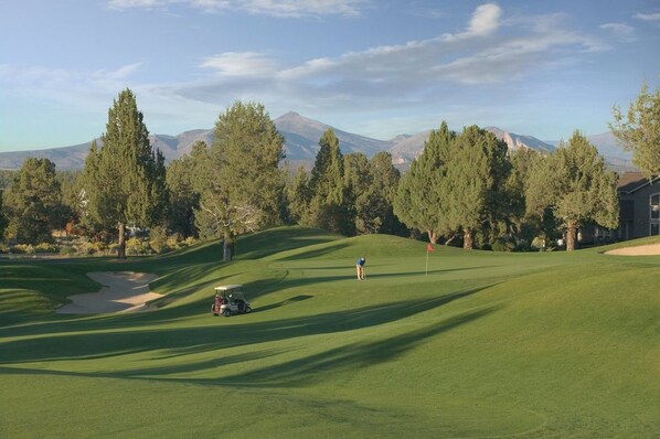 A golf course with a clubhouse, trees, and mountains in the background.