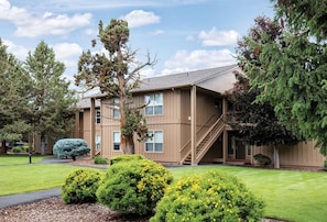 A multi-story building with a staircase leading to the entrance, surrounded by well-maintained lawns and various trees. - Redmond | High Desert Scenic Stay | Pool + Trails | 2BR Upper Floor (Redmond)