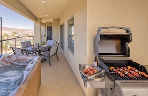 A balcony with a grill, a hot tub, and a dining area with chairs and a table. - St George | Elevated Red Rock Retreat | Pool + Hot Tub | 3BR Sleeps 6 (St. George)
