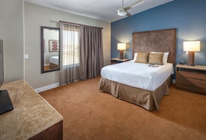 A hotel room with a bed, two bedside tables with lamps, a ceiling fan, a large mirror, and a window with curtains. - St George | Elevated Red Rock Retreat | Pool + Hot Tub | 3BR Sleeps 6 (St. George)