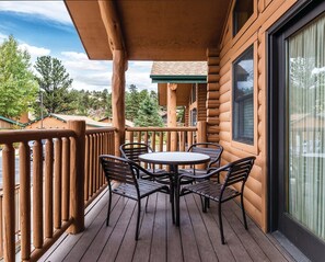 Eine Holzterrasse mit rundem Tisch und Stühlen, einer Glastür und Blick auf die umliegende Landschaft.