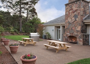 Un patio con mesas de picnic, chimenea de piedra y una parrilla.