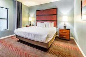 Habitación de hotel con una cama grande, dos mesitas de noche con lámparas, una alfombra estampada y un ventanal con cortinas.