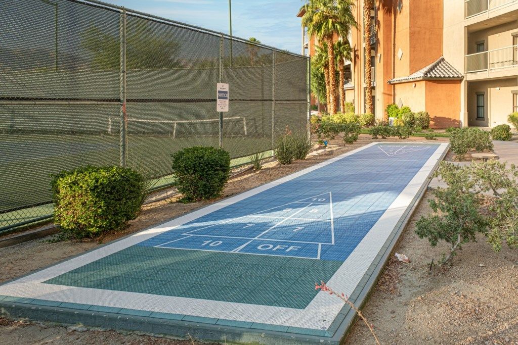 A shuffleboard court adjacent to a building with a mesh fence and a sign.
