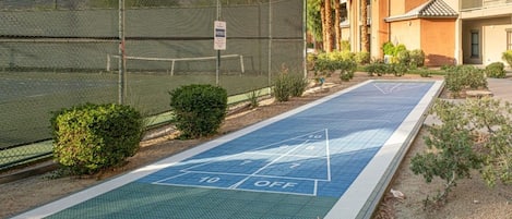 A shuffleboard court adjacent to a building with a mesh fence and a sign.