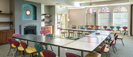 A conference room with a long table, colorful chairs, a fireplace, and large windows.