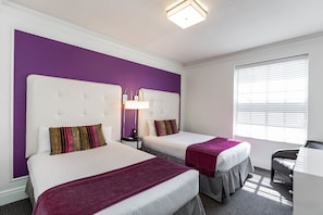 Une chambre d’hôtel avec deux lits, un bureau et une fenêtre avec des stores.