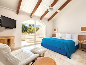 Una camera d'albergo con un letto, una TV, una sedia, un tavolo, una ventola a soffitto e vista sull'esterno.
