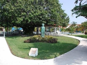 Una estàtua en una zona enjardinada amb un camí pavimentat i una piscina al fons.