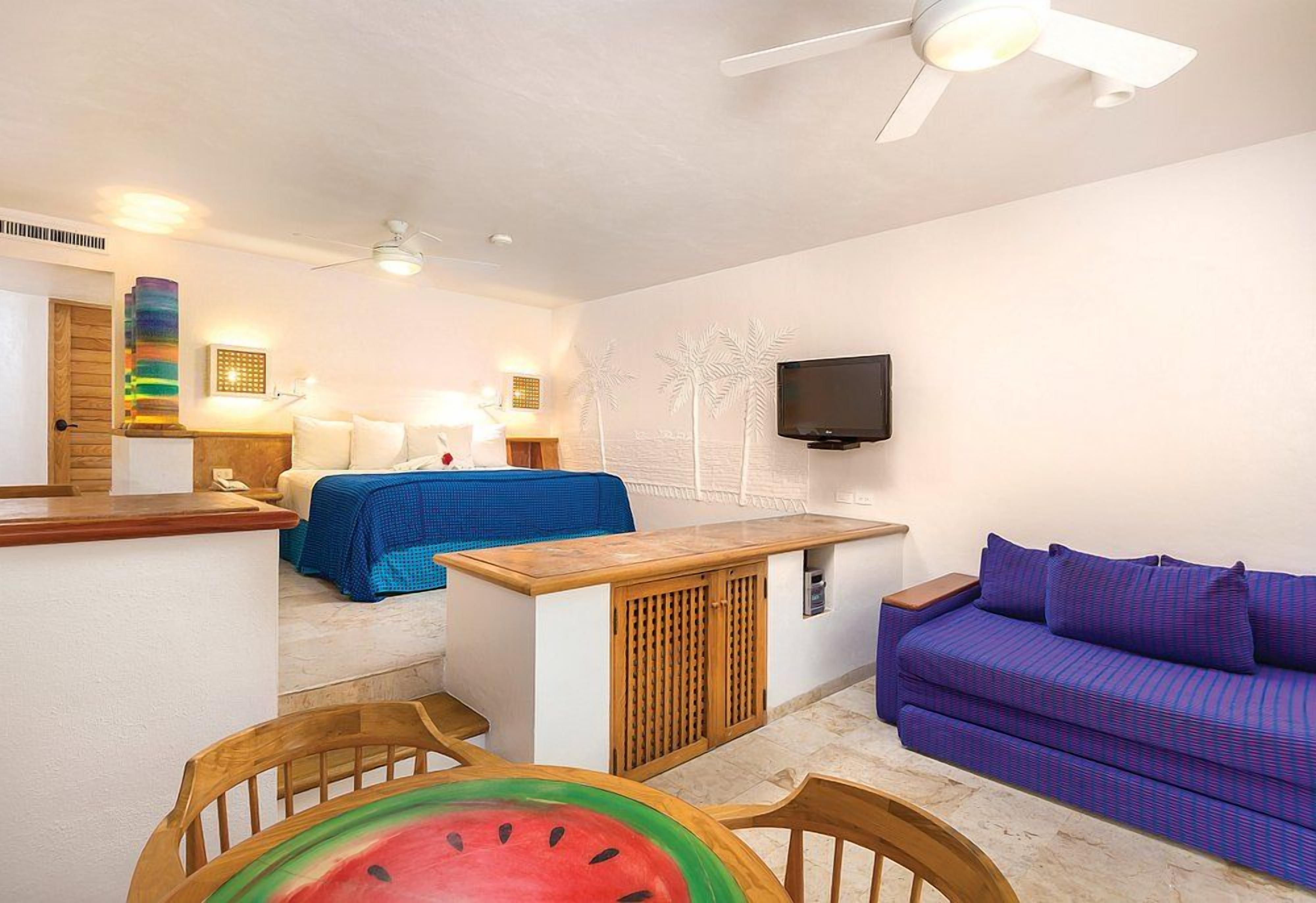 A compact living space with a kitchenette, a bed, a sofa, and a television.