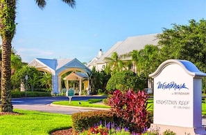 Una entrada de hotel con un porche cubierto, un letrero que dice 'WorldMark Wyndham Kingstown Reef at Orlando', y jardines bien cuidados.