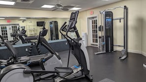 Un gimnasio con equipo de ejercicio, un espejo y una puerta con la señalización 'EXIT'.