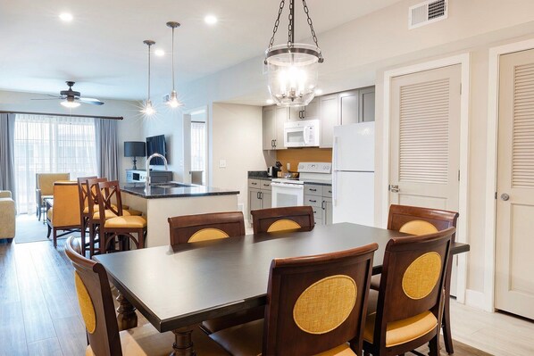 A modern kitchen with white appliances, a dining area with wooden chairs, and a ceiling fan. - Orlando | Friends & Family Park Getaway | Pool + Hot Tub | 2BR (Orlando)