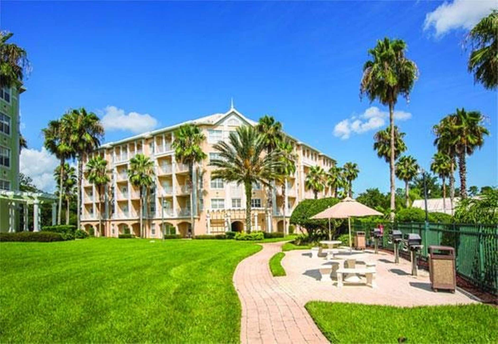 A large building with multiple balconies, a well-maintained lawn, and a paved walkway leading to outdoor seating.