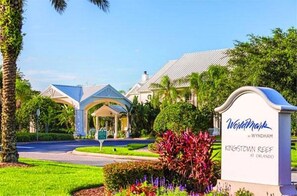 Een hotelingang met een overdekt terras, een bord waarop 'WorldMark Wyndham Kingstown Reef at Orlando' staat, en verzorgde beplanting.