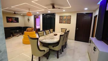 Un comedor con una mesa redonda y sillas, un sofá y un taburete decorativo color naranja.