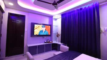 Un dormitorio moderno con una cama, un televisor montado en la pared, un ventilador de techo y una puerta de color oscuro.