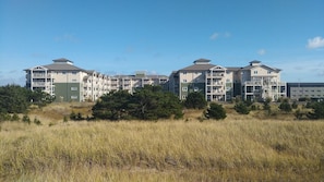 A multi-story residential building with balconies, surrounded by grassy fields and sparse trees. - Long Beach WA | Romantic Coastal Retreat | Pool + Hot Tub (Long Beach)