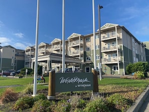 Un edificio de varios pisos con balcones, un letrero que dice 'Wynham by Wyndham', y un estacionamiento al frente.