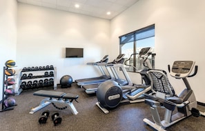 Un gimnasio con cintas de correr, elípticas, una banca y un estante con mancuernas.