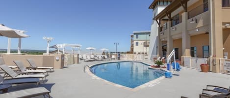 Un área de piscina con sillas de descanso, una piscina y un edificio con balcones.