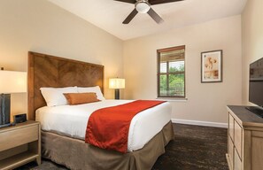 Habitación de hotel con cama, mesita de noche, escritorio, televisor, ventilador de techo y ventana con persianas.