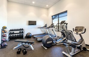 Ein Fitnessraum mit Laufbändern, Crosstrainern, einer Bank und einem Hantelgestell.