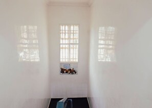 Una habitación con ventana, un estante con objetos y un objeto negro en el suelo.