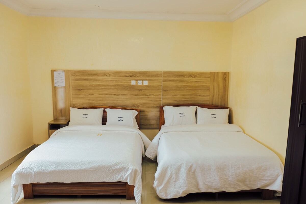 A double room with two beds, wooden headboard, white bedding, and a wooden nightstand with a paper on it.