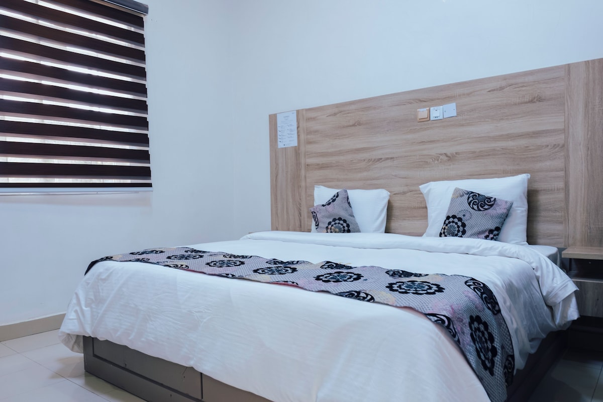 A modern bedroom with a bed, wooden headboard, and a window with blinds.