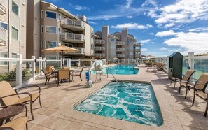 Un espace piscine doté de chaises longues et d’un jacuzzi, entouré d’immeubles à plusieurs étages avec des balcons.