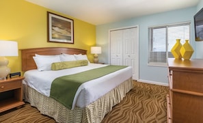 Une chambre d’hôtel comprenant un lit, des tables de chevet, une commode, une fenêtre avec des stores et une porte.