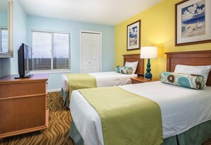 Quarto de hotel com duas camas, uma televisão, um abajur e uma janela com persianas.