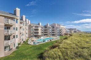 Uma fileira de edifícios com várias andares, varandas, piscina e área gramada.