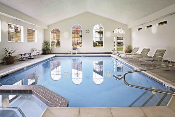 Una piscina interior amb parets de vidre transparent, un paviment de rajoles i seients per relaxar-se.