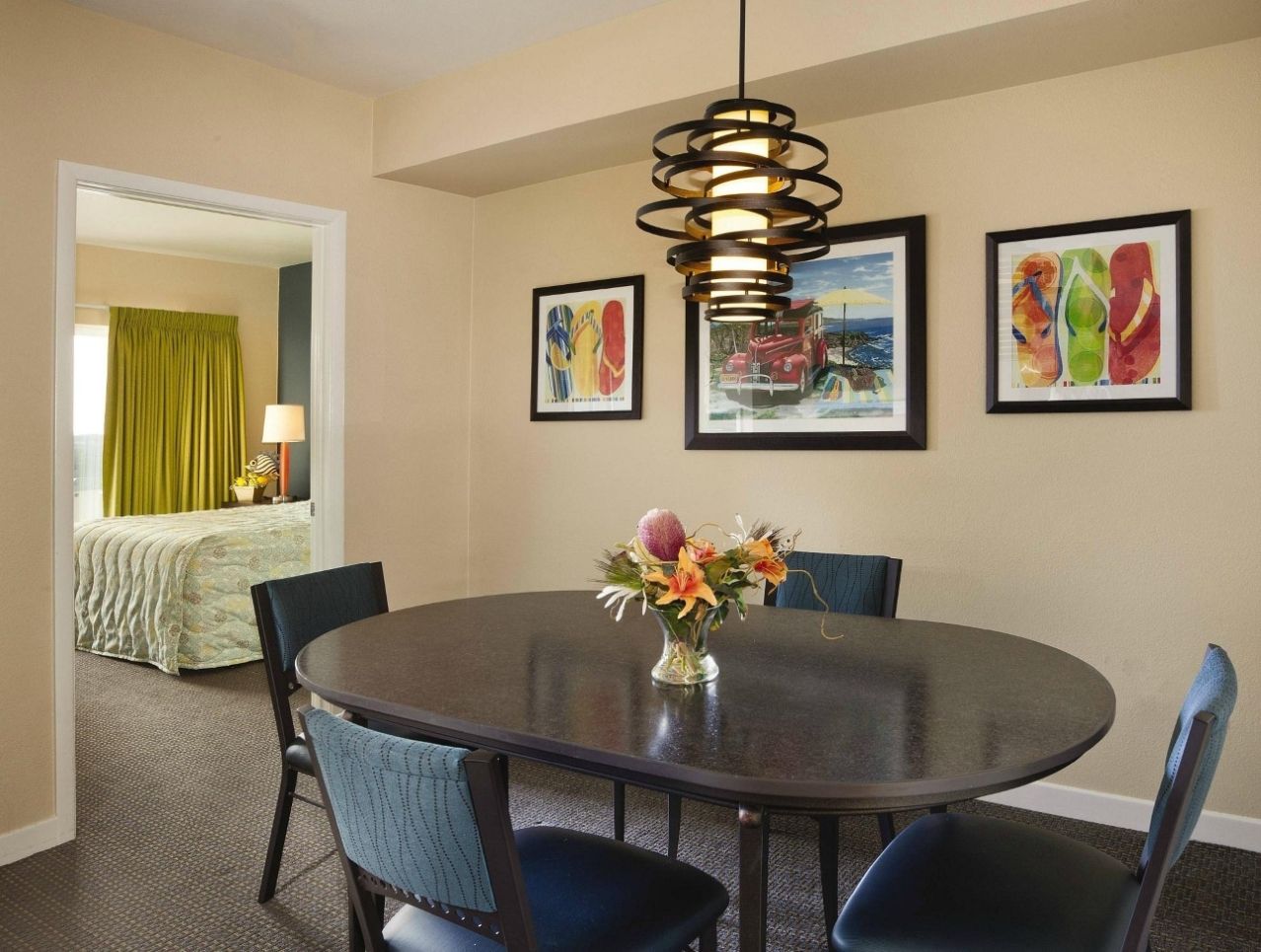 A hotel dining area with a round table, chairs, a vase of flowers, and framed artwork on the walls.