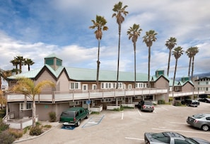 A motel with a long building, multiple parking spaces, and palm trees.