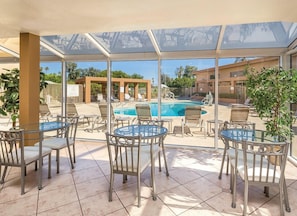 A glass-enclosed outdoor area with a pool, lounge chairs, and tables. - Palm Springs | Couples Desert Retreat | Pool + Hot Tub (Palm Springs)