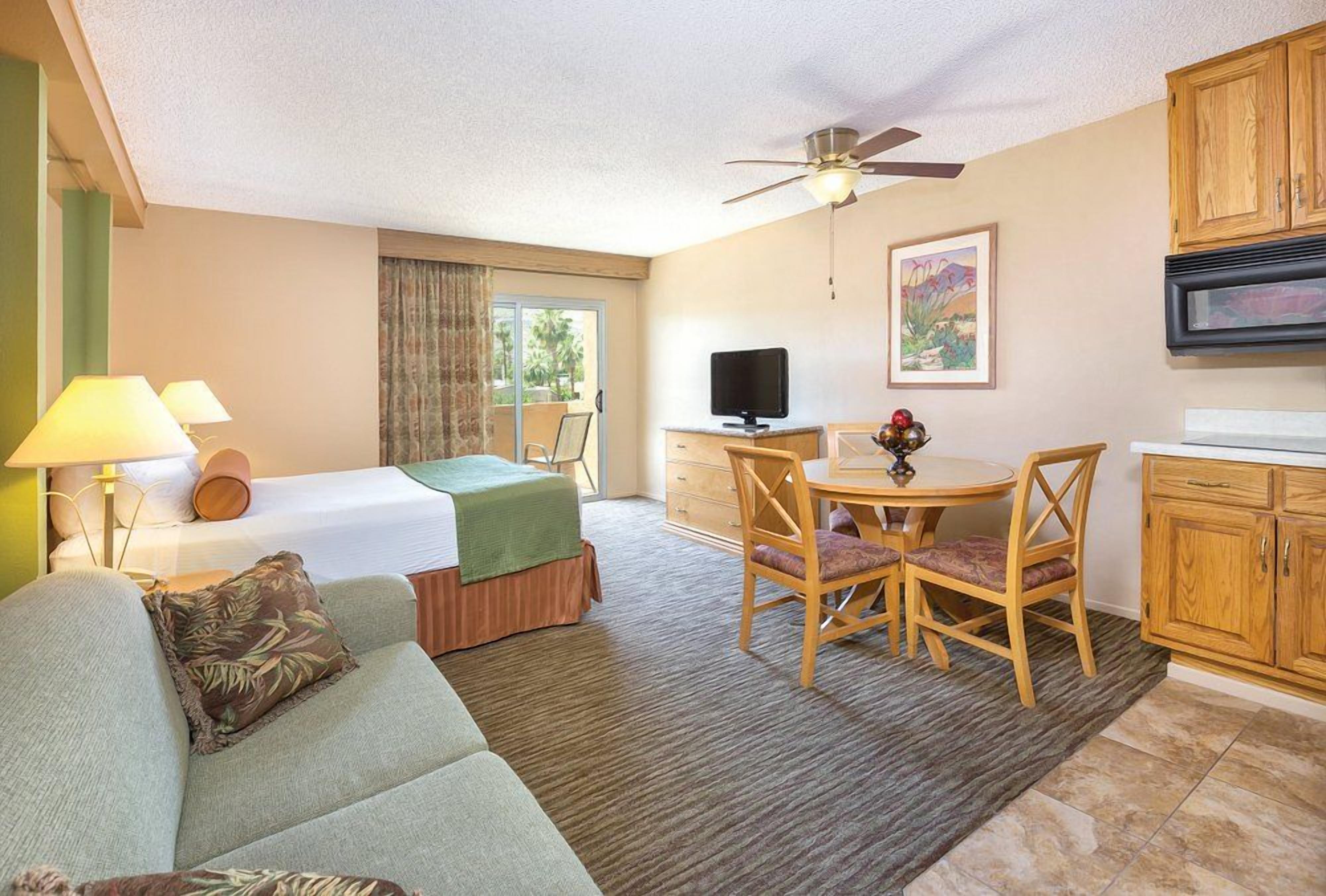 Une chambre d’hôtel comprenant un lit, un canapé, une table à manger avec des chaises, un téléviseur et des armoires en bois.
