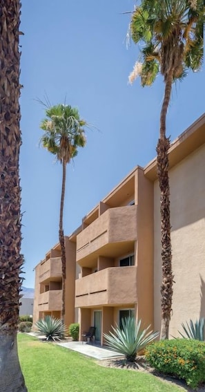 A multi-story building with balconies, surrounded by palm trees and agave plants. - Palm Springs | Couples Desert Retreat | Pool + Hot Tub (Palm Springs)