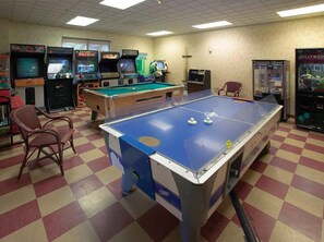 A pool table with surrounding arcade machines, a pool table, and a poster on the wall. - Klamath Falls | Romantic Golf Retreat | Pool + Golf (Klamath Falls)