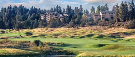 Un campo de golf con un estanque, rodeado de colinas boscosas y edificios.